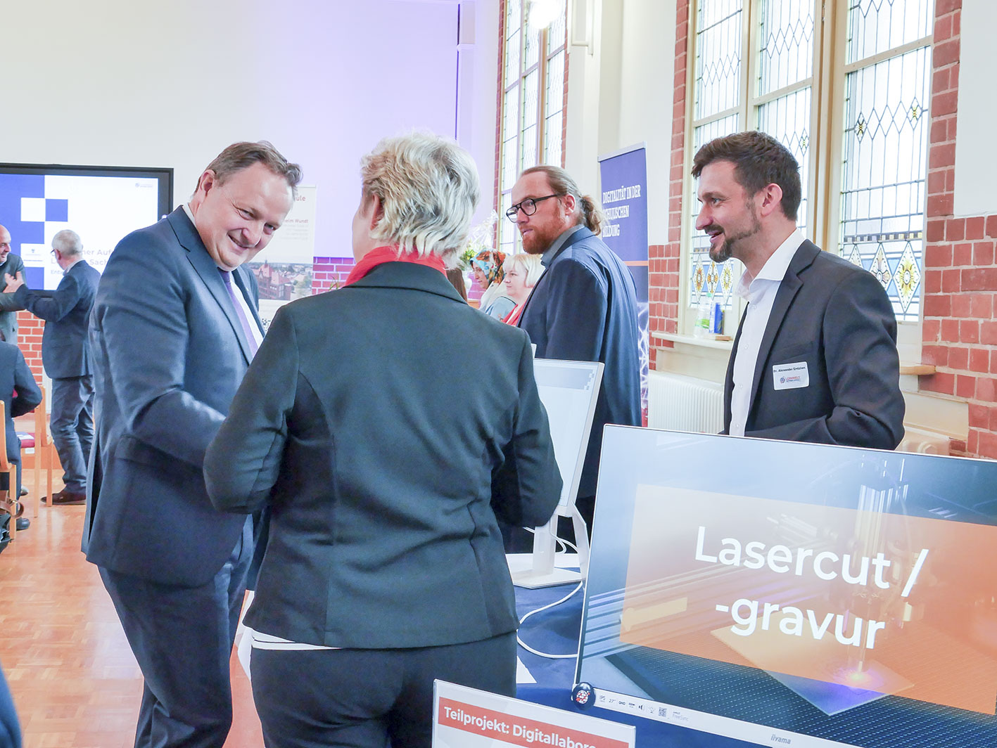 Staatssekretär Böhm (links) im Gespräch mit Teilnehmenden beim Projektstart „Lernwelt Sachsen-Anhalt“ am 02.04.2025 in der Wilhelm-Wundt-Gemeinschaftsschule Tangerhütte; im Vordergrund ist eine Station zum Thema Lasercut und Gravur zu sehen.